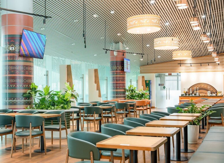 A modern indoor dining area with green chairs, wooden tables, and hanging pendant lights. 3