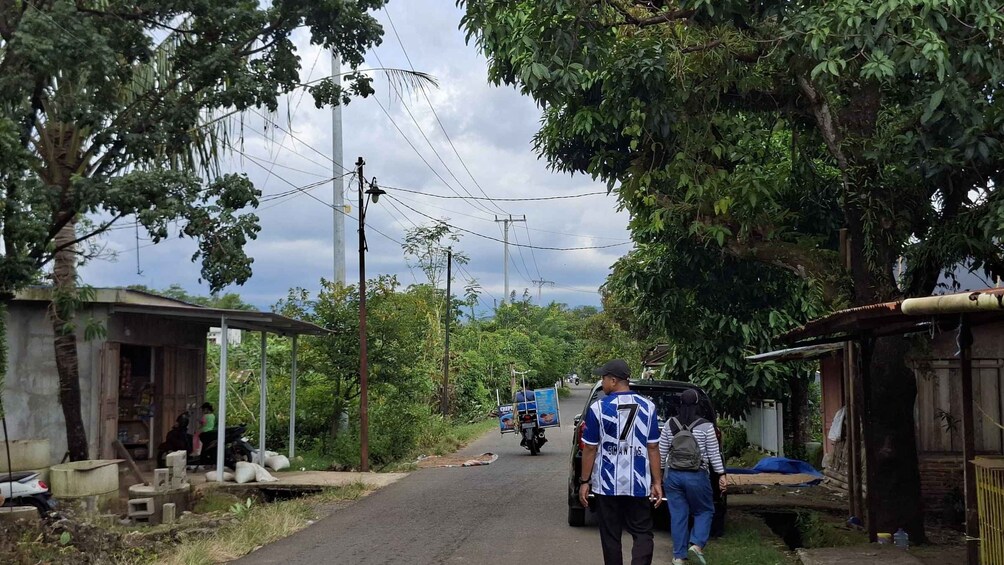 A rural road with a motorcycle and a car, surrounded by greenery and small buildings. 3
