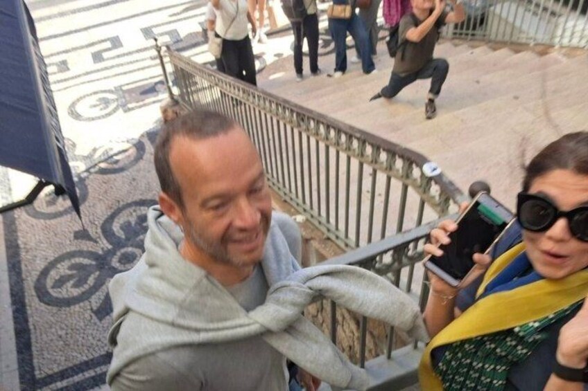 A person in a grey hoodie and a woman in a yellow and green outfit standing near a metal railing. 3