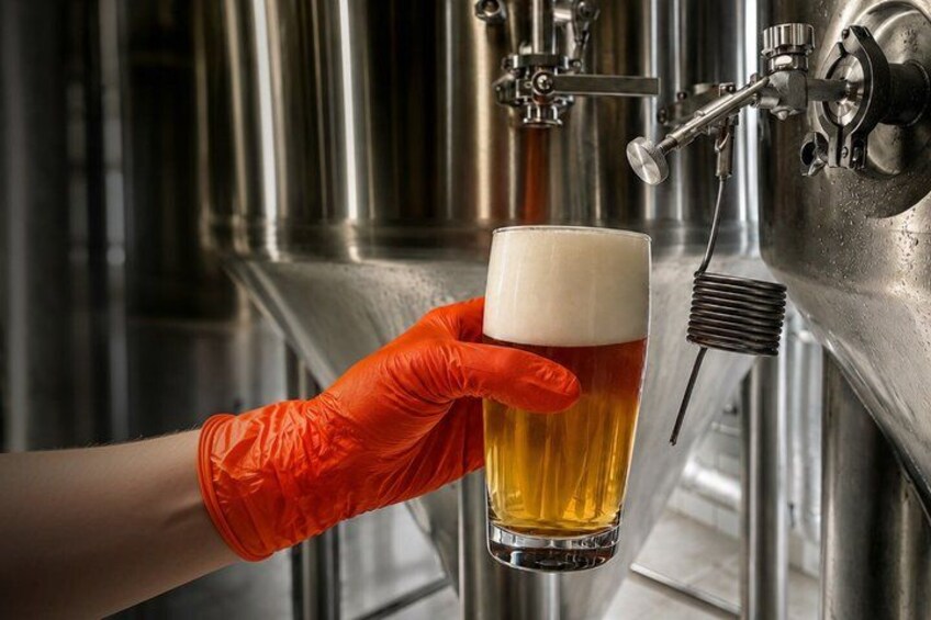 A person wearing an orange glove holding a glass of beer near a tap. 1