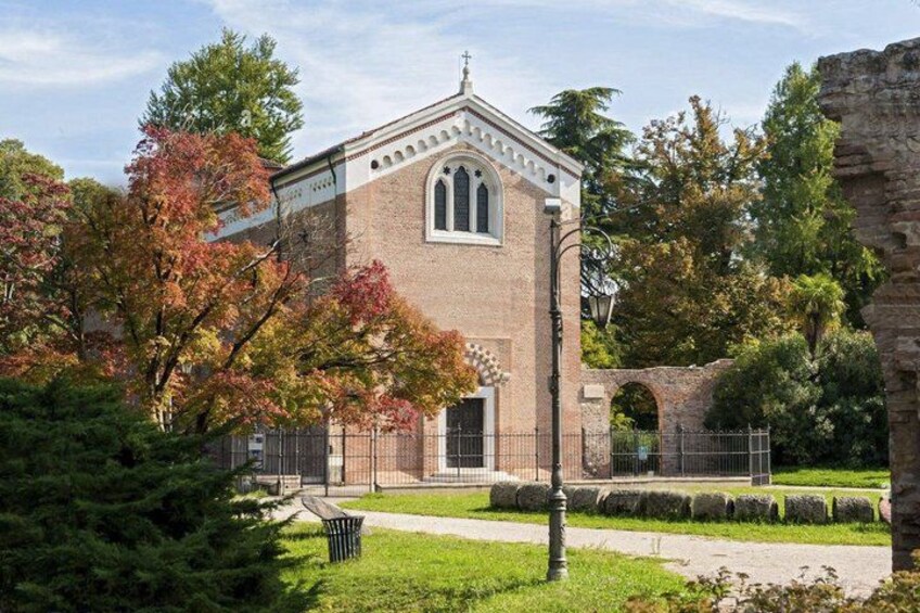 A brick building with a pointed roof and arched windows, surrounded by trees and a pathway. 4