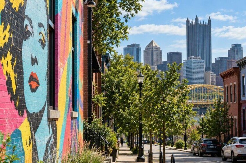 A city street with a colorful mural, trees, a bridge, and a skyline in the background. 2