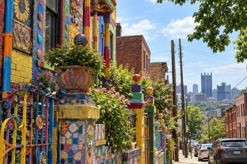 A colorful street with a decorative fence, a city skyline in the background, and parked cars. 1