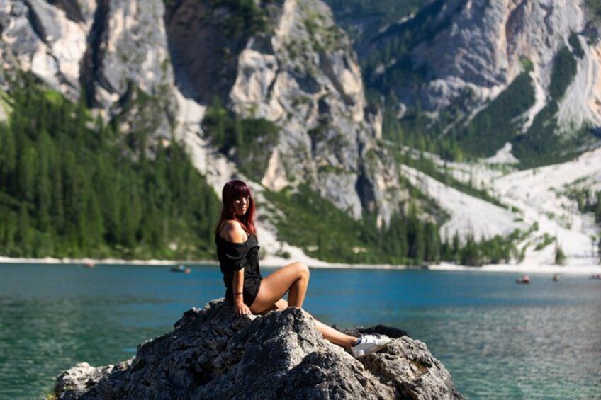 A person sitting on a rock by a lake with mountains in the background. 2