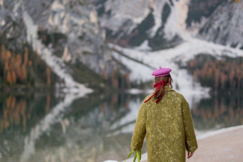 A person in a green coat and pink hat walking near a snowy mountain. 5