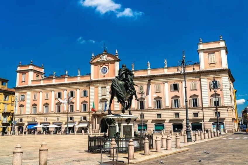 A historic building with a statue in front, a clear blue sky, and a paved square. 5