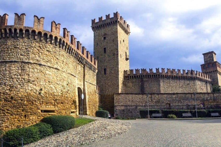 A historic stone castle with a tall tower, a fortified wall, and a paved courtyard. 1