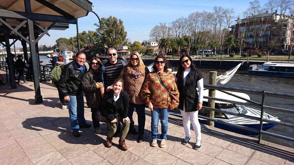 A group of people standing on a waterfront promenade with a river and boats in the background. 3