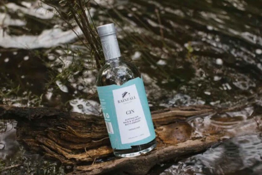A bottle of Rainfall Gin placed on a log by a stream. 2