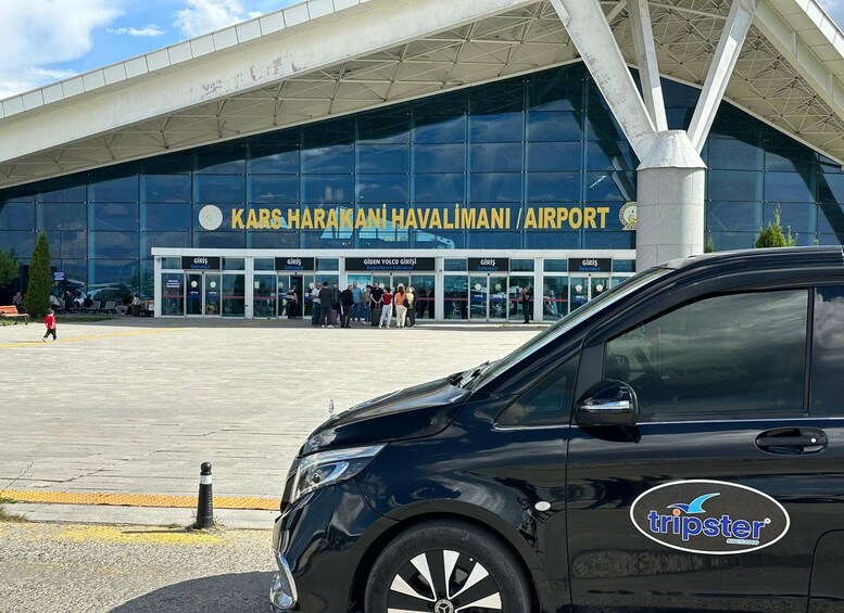 A modern airport terminal with a glass facade and a sign reading 'Kars Harkani Havalimani Airport'. 2