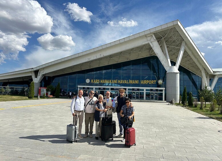 A group of people standing in front of Kars Harakani Havalimani Airport with their luggage. 3