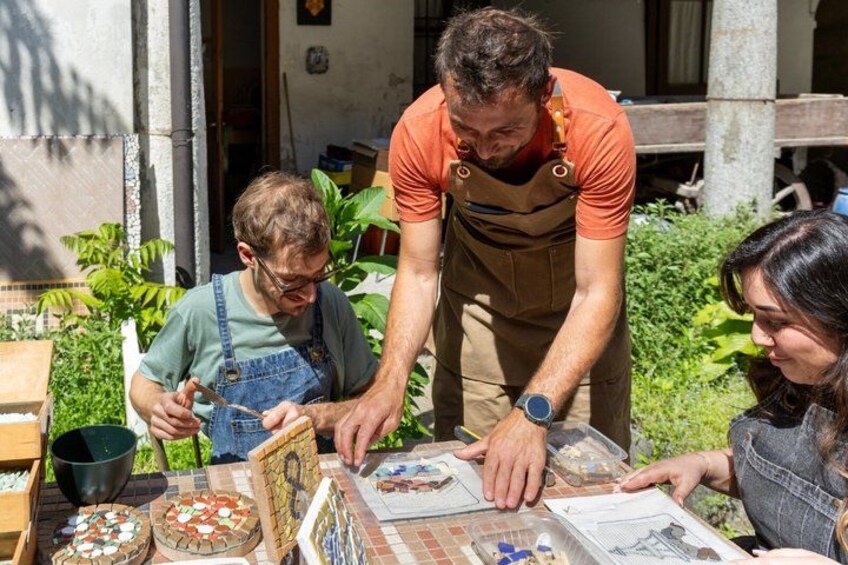 Three people working on a mosaic project outdoors with tiles and tools. 1