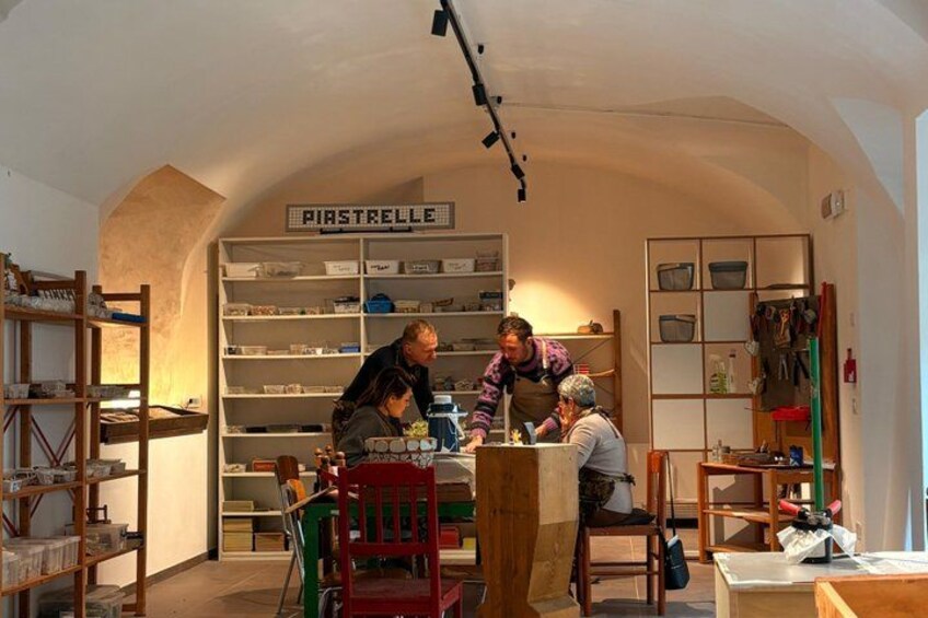 A kitchen with a sign reading 'PIASTRELLE,' shelves with kitchenware, and people engaged in cooking activities. 4