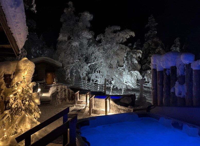 A snow-covered outdoor area with a hot tub, wooden structures, and snow-covered trees at night. 2