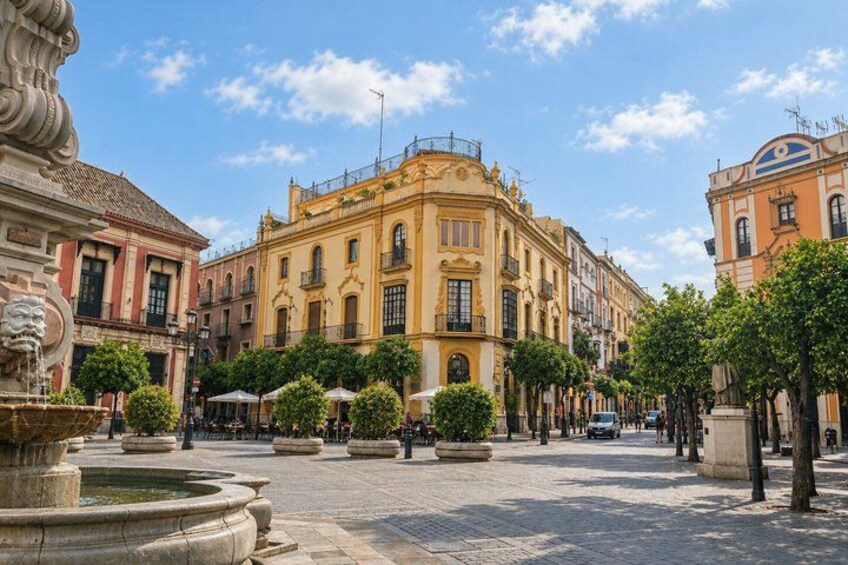 A historic square with ornate buildings, a fountain, and trees. 2