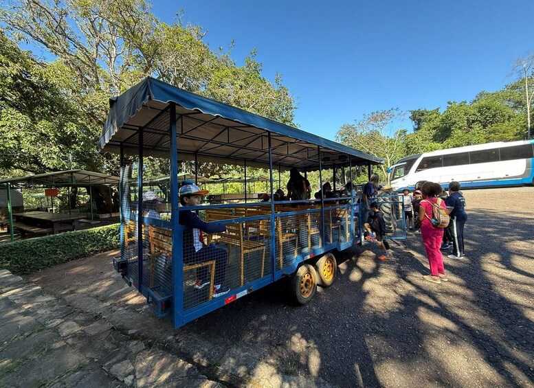 A blue trolley with a metal cage, parked on a paved area with trees in the background. 1