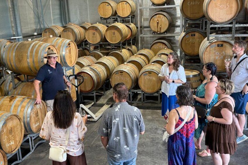A group of people in a wine cellar surrounded by wooden barrels. 1