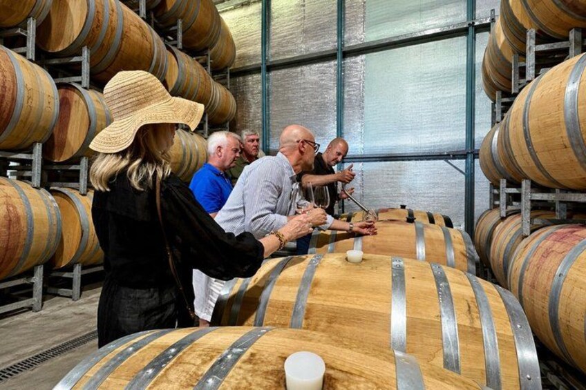 A group of people inspecting large wooden barrels in a warehouse. 2