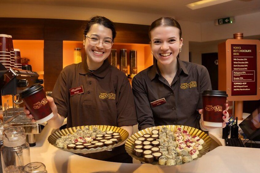 Two individuals holding trays of assorted pastries and coffee cups in a café setting. 3