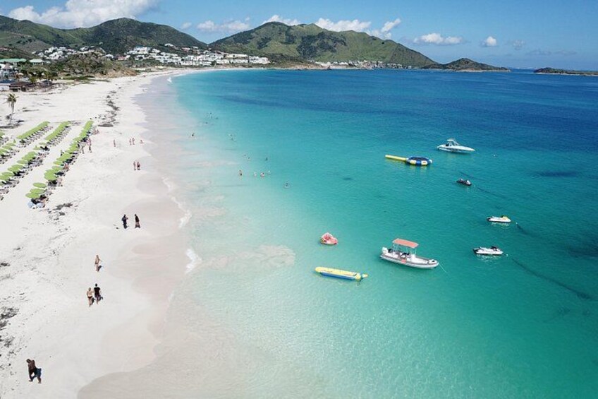 A beach with clear turquoise waters, several boats, and people walking along the shore. 3
