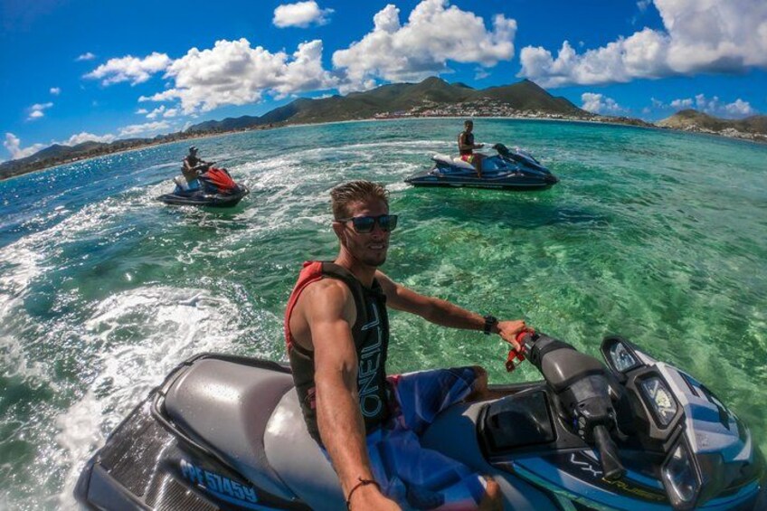 A person riding a jet ski on clear turquoise water with mountains in the background. 1
