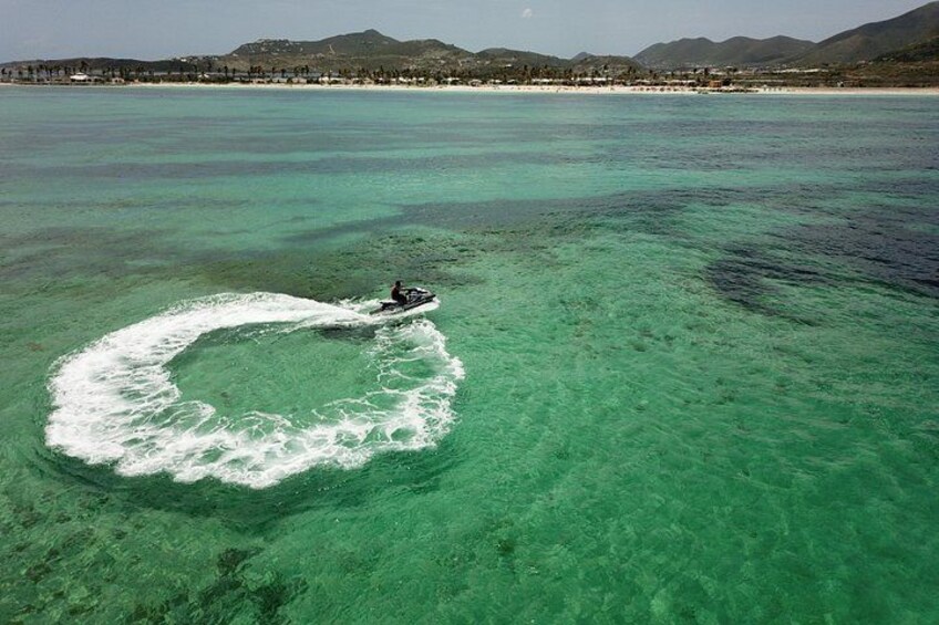 A jet ski creating a wake in turquoise water with a beach and mountains in the background. 5