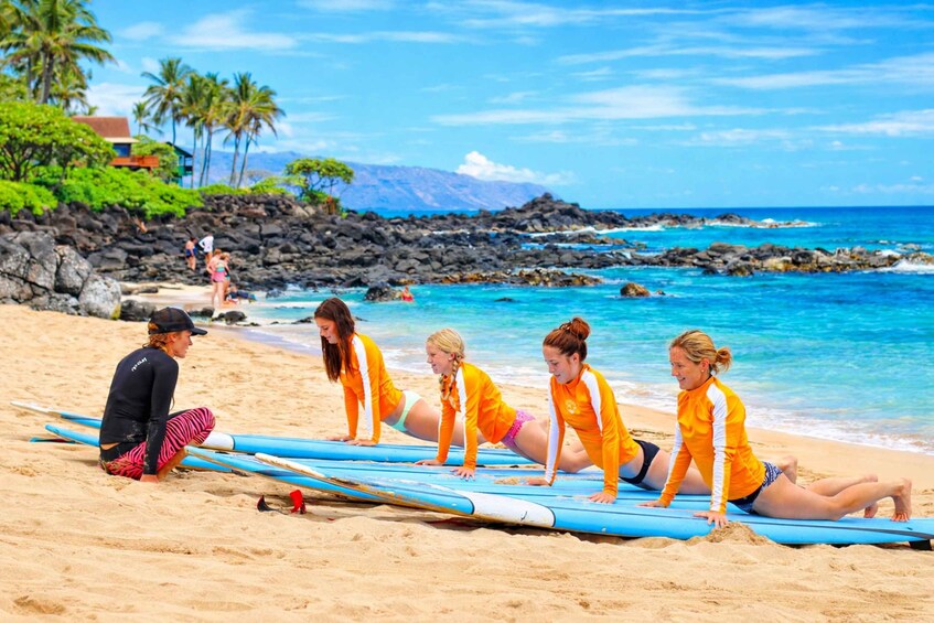A group of people on a beach with surfboards, palm trees, and a rocky shoreline. 1