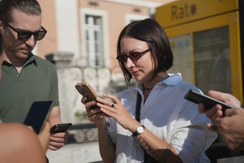 A person using a smartphone, another person holding a tablet, and a yellow vehicle with the word 'Rato' visible in the background. 2