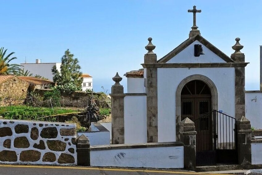 A small white church with a cross on top, a stone wall, and a statue. 1