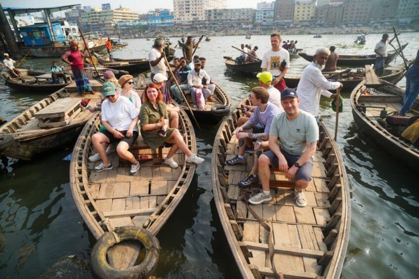 People on wooden boats on a river with buildings in the background. 2
