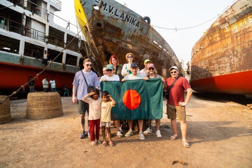 A group of people standing in front of a rusted ship with the name 'M.V. LANKA' on it. 1