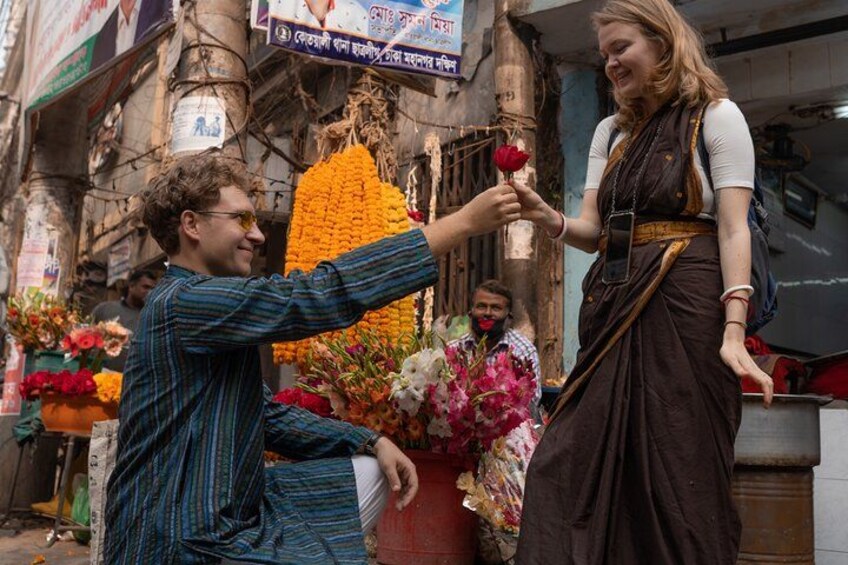 A street market with flowers and a person giving a rose to another person. 4