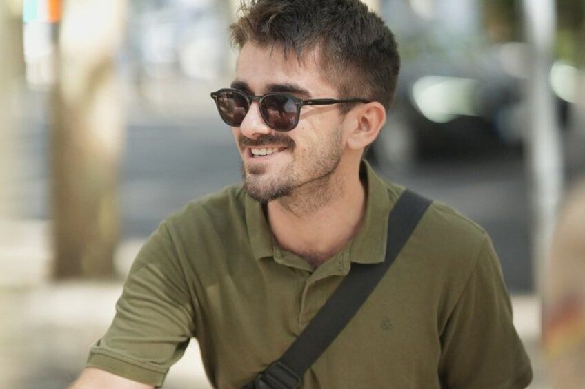 A person wearing a green shirt with a shoulder strap, sitting outdoors. 4