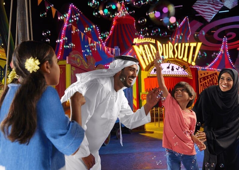 A group of people at a themed attraction with a sign reading "Madagascar Mad Pursuit!" 3