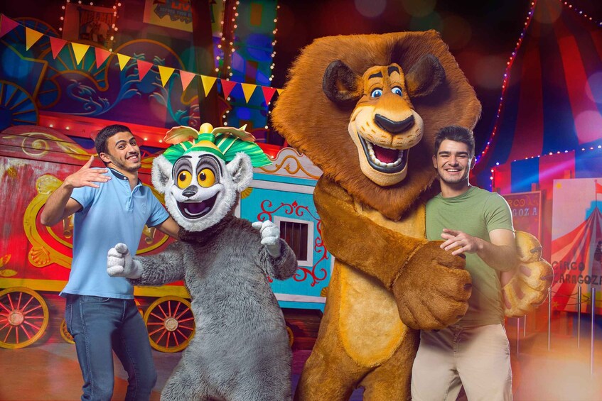 A man in a blue shirt and another in a green shirt posing with a lion and a lemur mascot. 2