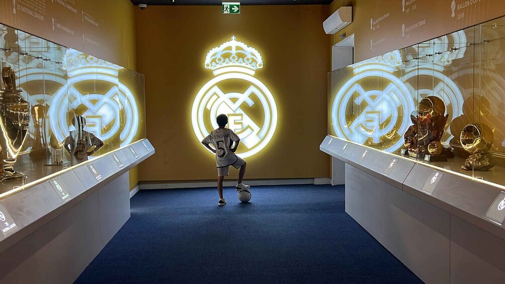 A person in a football jersey juggling a ball in front of illuminated Real Madrid logos. 1