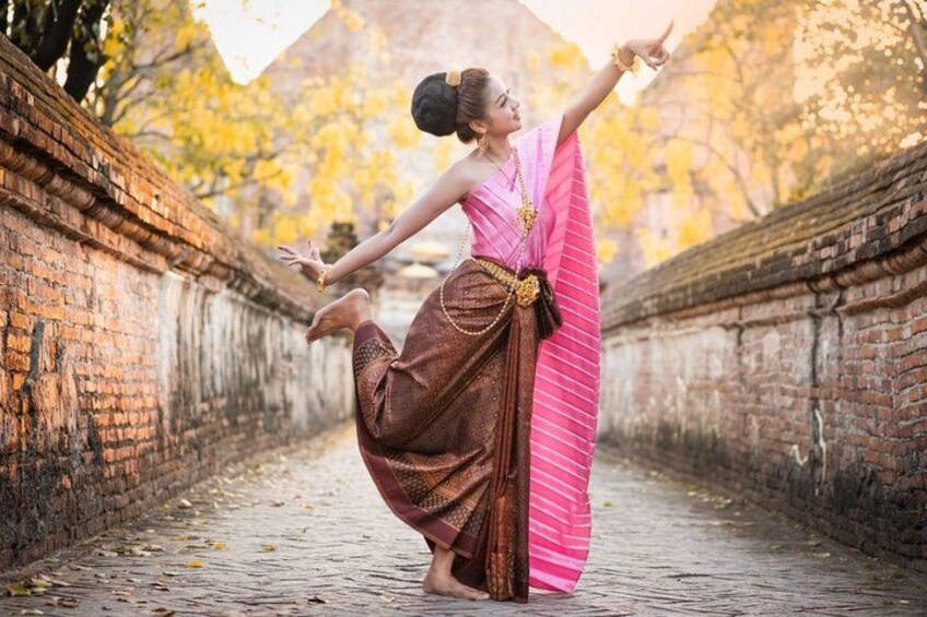 A person in traditional attire performing a dance in a historical setting with brick walls and autumn foliage. 5