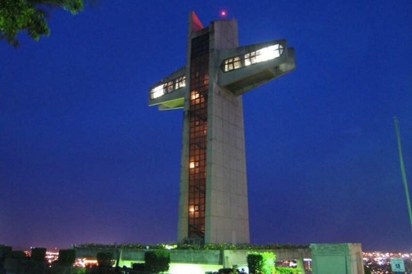 A tall, illuminated building with a unique design, surrounded by greenery and city lights in the background. 4