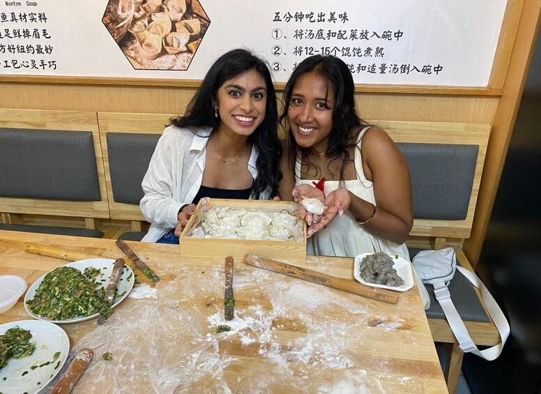 Two individuals at a table with dumplings, a wooden bench, and a menu with Chinese characters. 1