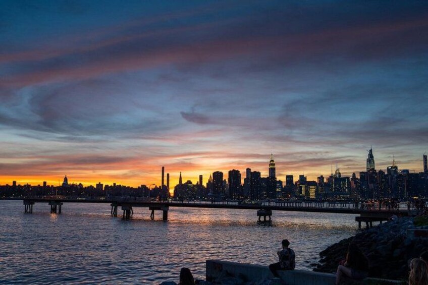 A city skyline at sunset with a bridge over water. 1