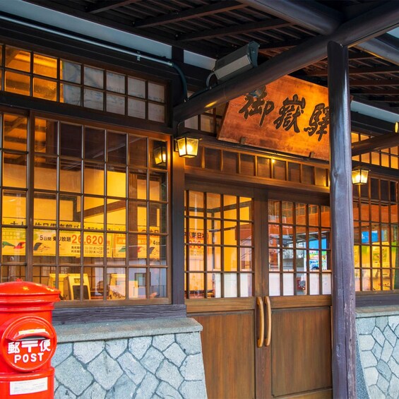A traditional Japanese building with wooden doors and windows, a stone wall, and a red post box labeled 'POST'. 2