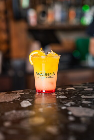 A glass of drink with a slice of orange and ice cubes on a bar counter. 4