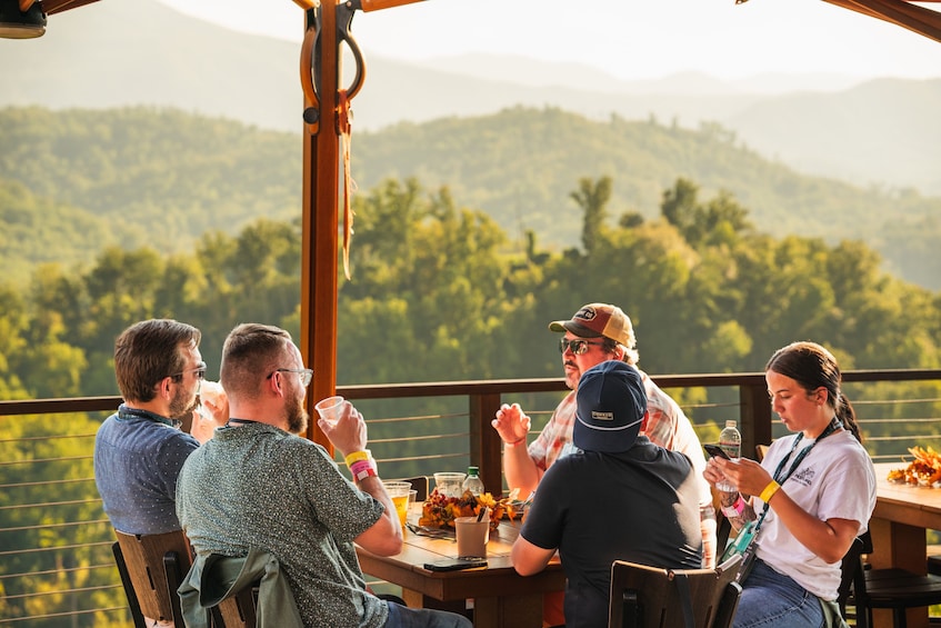 A group of people sitting at a table outdoors with a scenic view of hills and trees in the background. 3