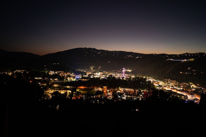 A nighttime cityscape with illuminated buildings and a mountain in the background. 5