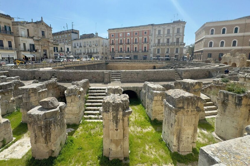 Antiche rovine con colonne in pietra e una struttura circolare, immerse in edifici storici. 4