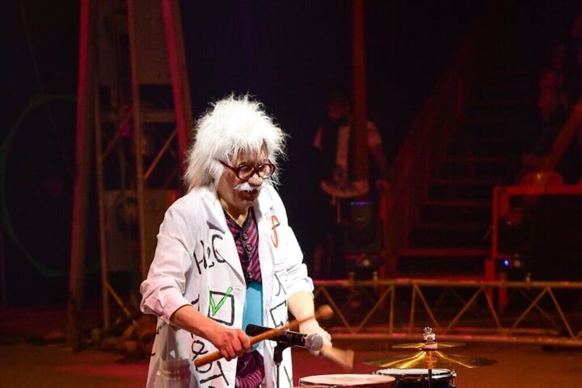 A person playing a drum set on a stage with a backdrop of a large structure. 3