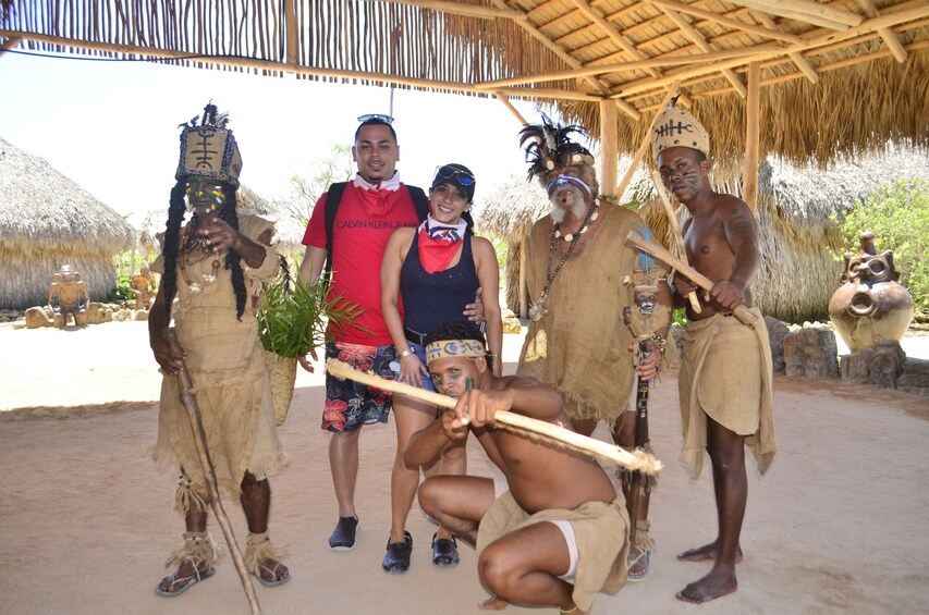 Tourists pose with men in traditional Dominican dress with large sticks