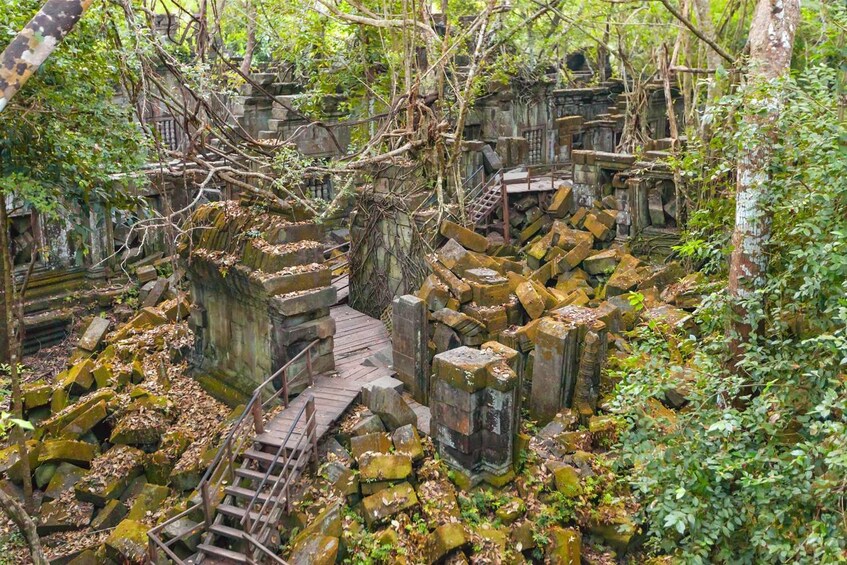 A dilapidated stone structure with overgrown vegetation and a wooden staircase. 5