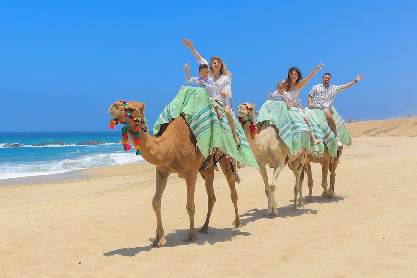 Un groupe de personnes chevauchant des chameaux sur une plage, avec l’océan en arrière-plan. 2