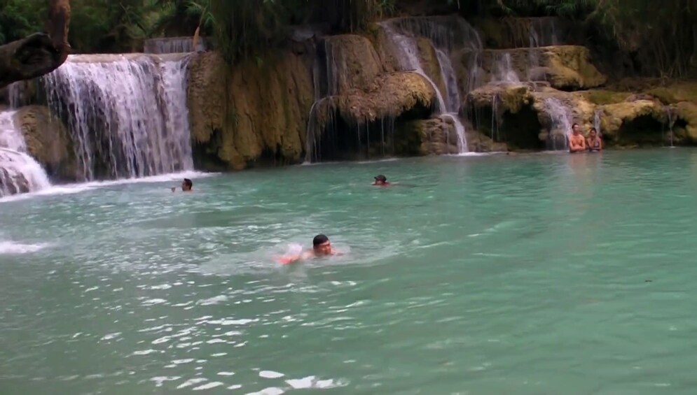 Tourists swim in pool below Kuang Si Waterfall